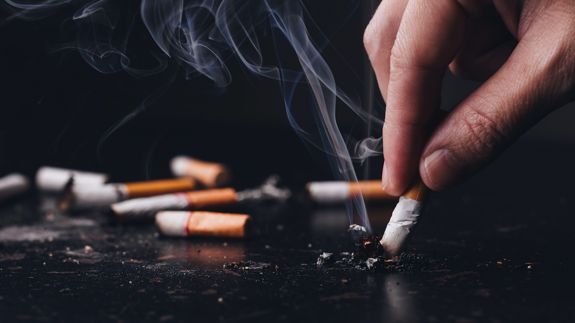 Cropped Hand Of Person Putting Out Cigarette Against Black Background smoking 271219 CREDIT ALAMY