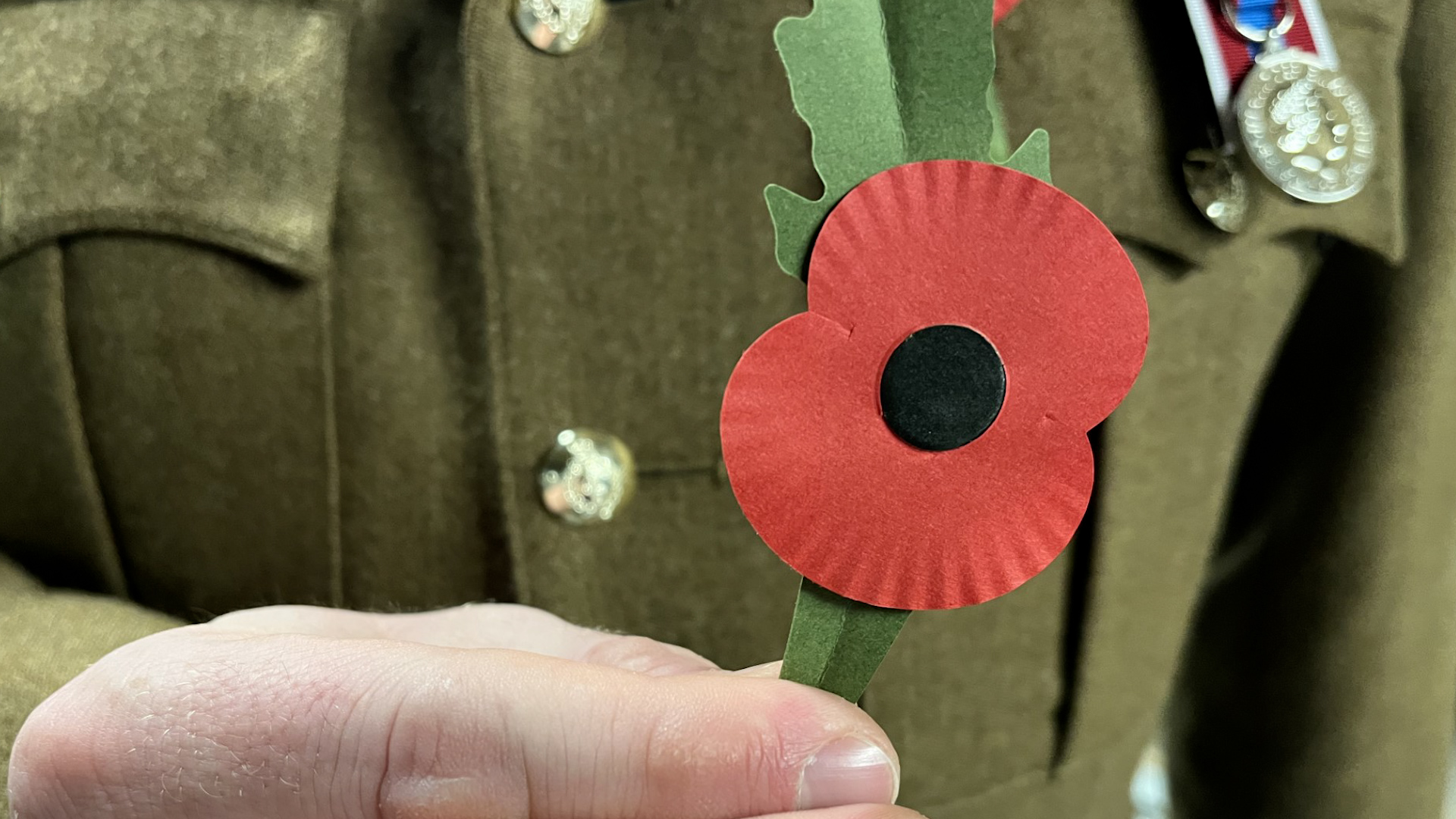 Member of the British Armed Forces holding up the RBL's new plastic poppy 261023 CREDIT BFBS