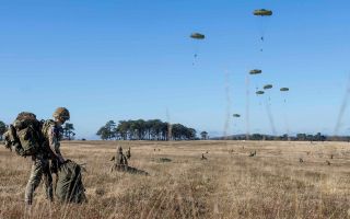 A soldier, with his bergen already on his back, packs away his parachute after landing on the drop zone